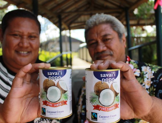 Two people smile while holding cans of Savai'i Popo Coconut Cream from Samoa, displaying a coconut on the label.