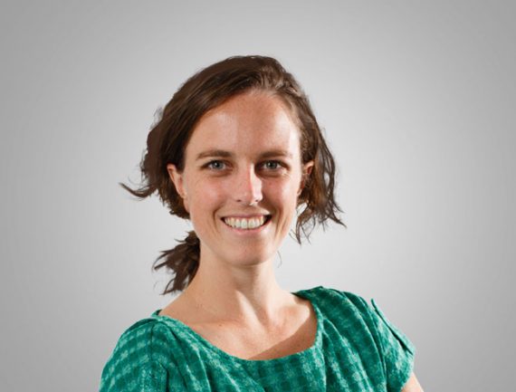 Smiling woman with brown hair in green shirt poses against grey background.