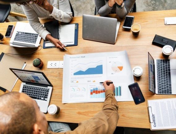 Business meeting with spreadsheet, charts, contract, and business strategy on laptop screen.