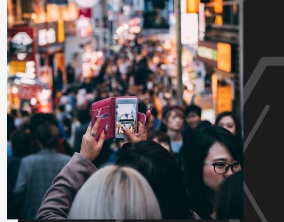Person in pink jacket takes photo of crowded Japanese street, woman in foreground.