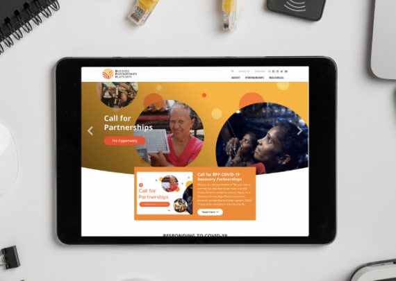 A tablet displaying the Business Partnerships Platform website with women from diverse backgrounds, surrounded by tech items on a white surface.
