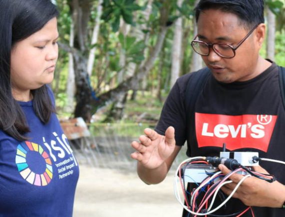 Man in Levi's shirt working on device as woman in blue shirt with logo watches.