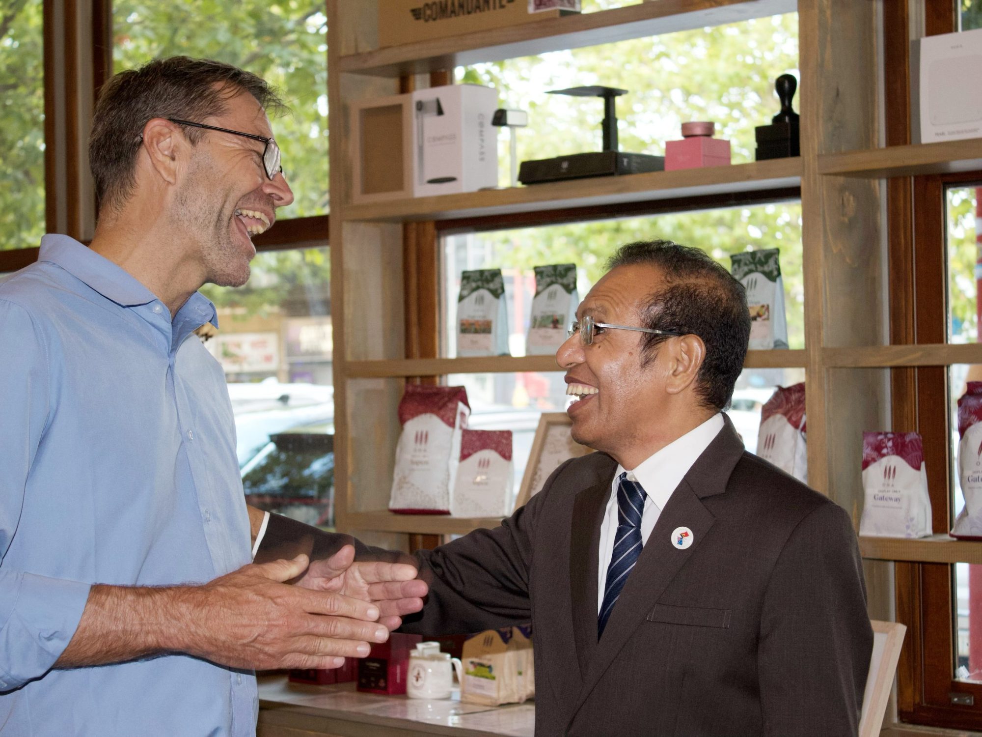 Men in a coffee shop, one in a light blue shirt, one in a dark suit.