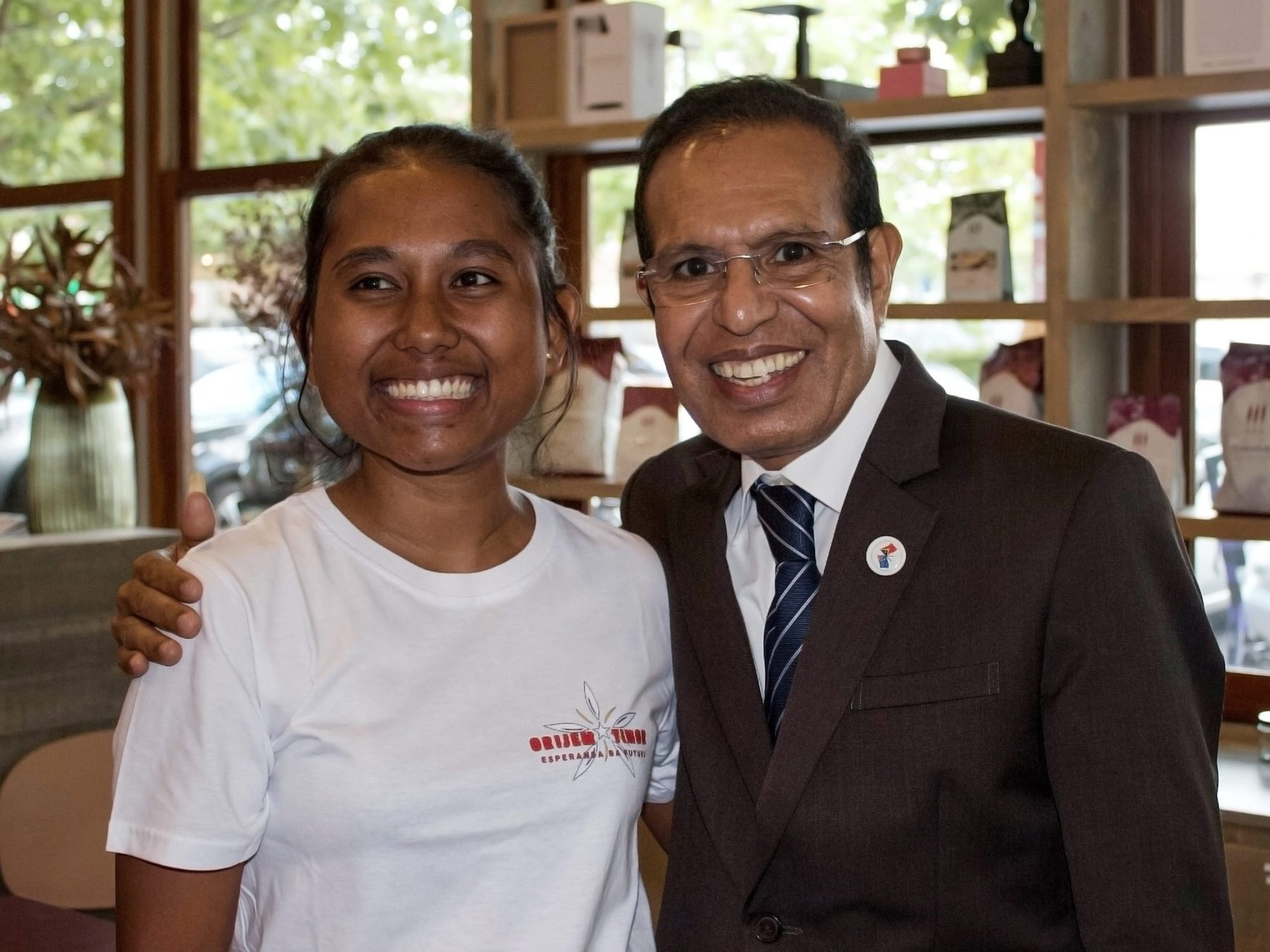 A man in a suit and a young woman in a white t-shirt smiling.