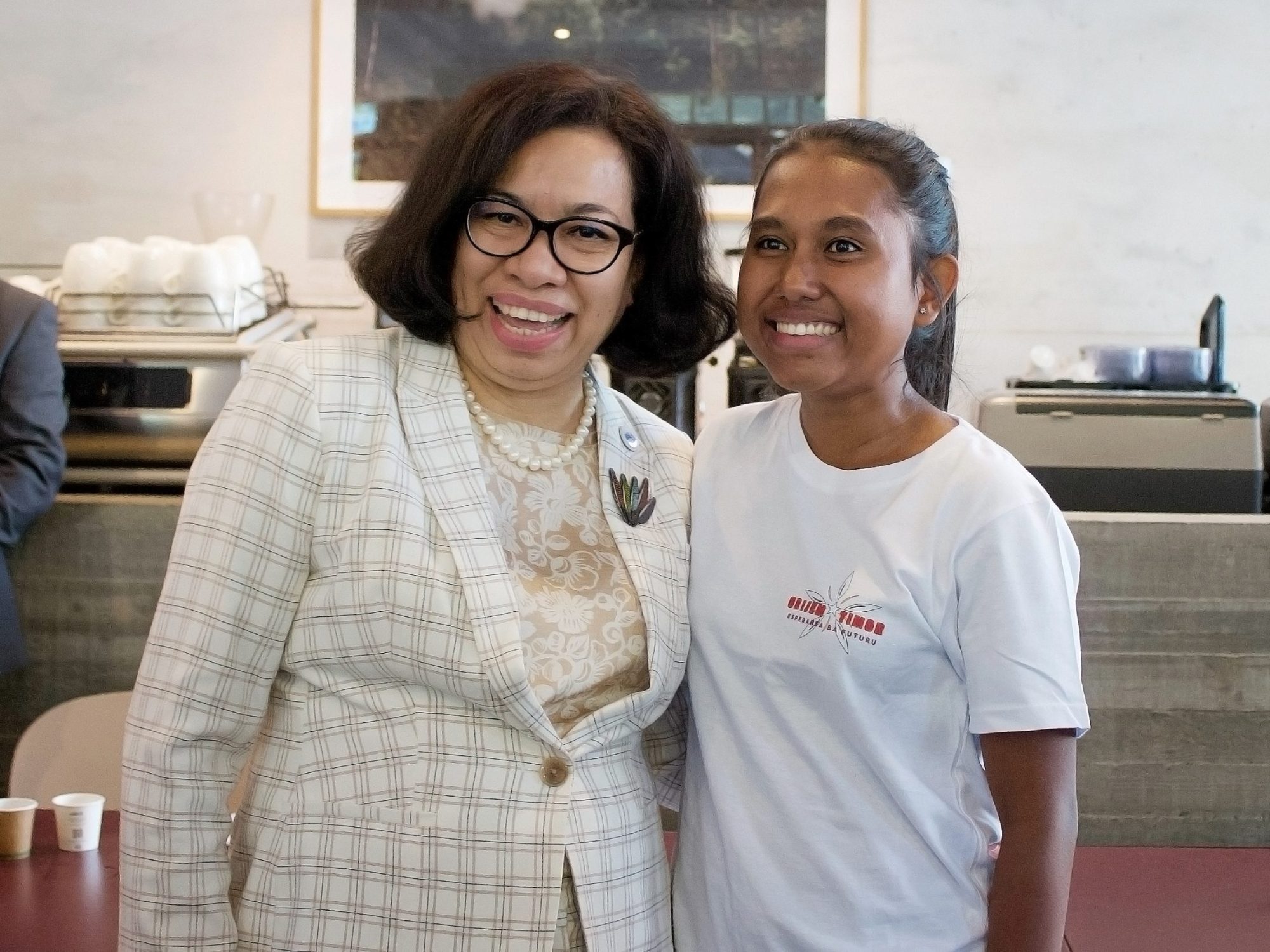 Smiling women, one in plaid blazer, the other in white t-shirt with text.