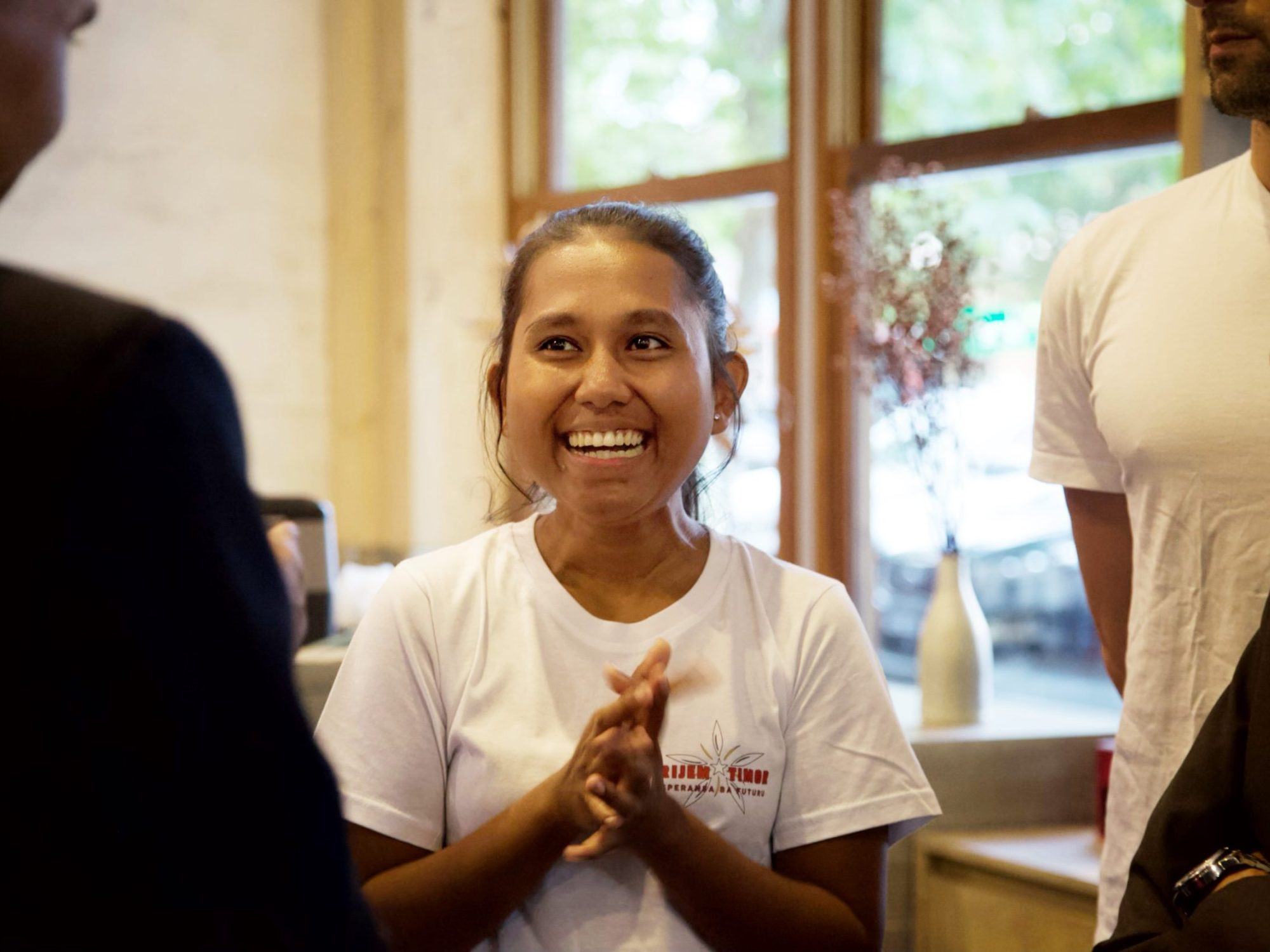 Woman wearing a logo tee among two men in a cafe setting.