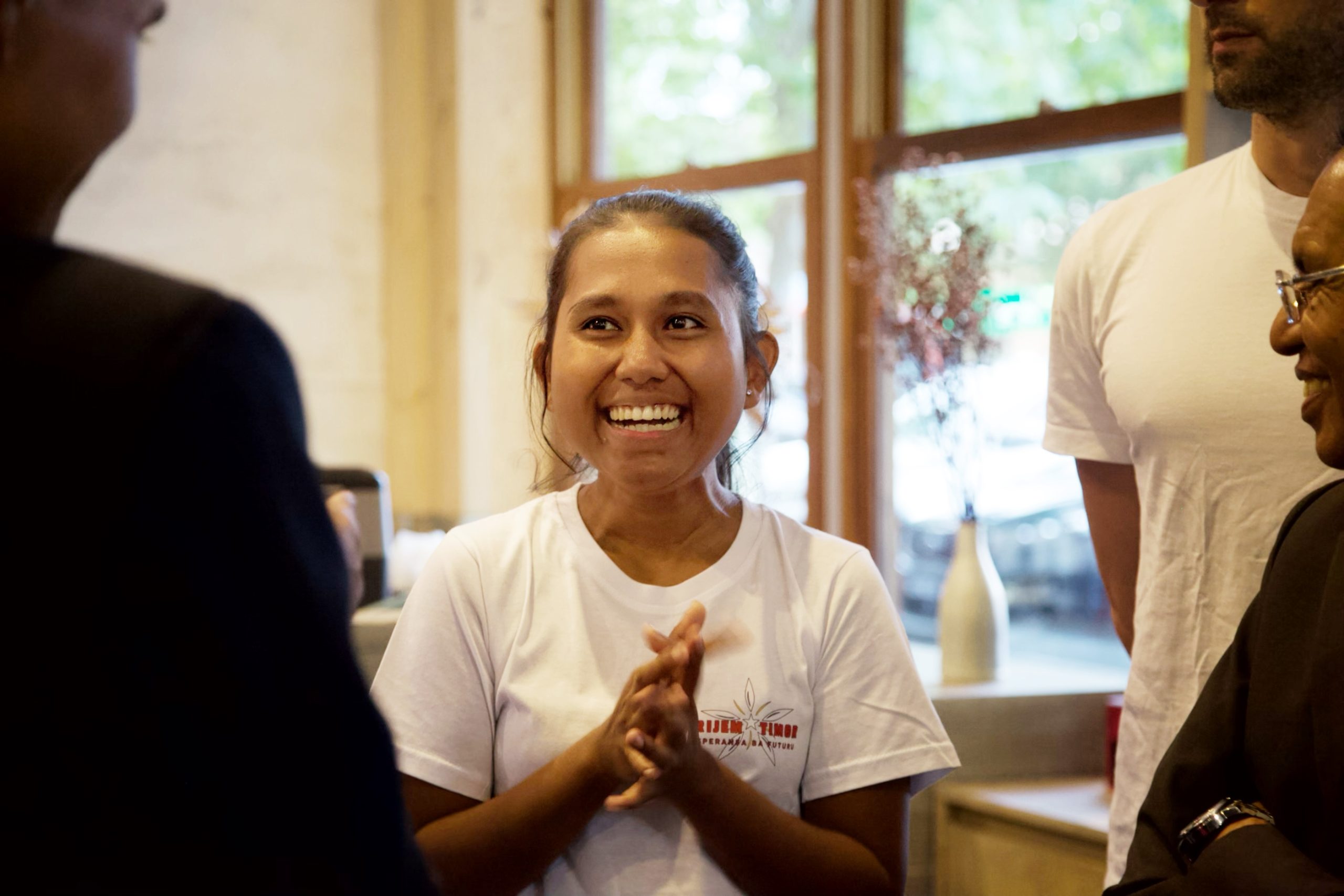 Woman wearing a logo tee among two men in a cafe setting.